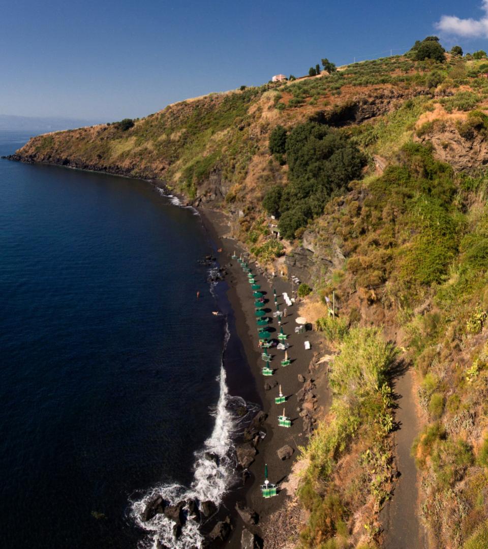 Spiaggia isolata con ombrelloni verdi, mare blu e scogliera verdeggiante.